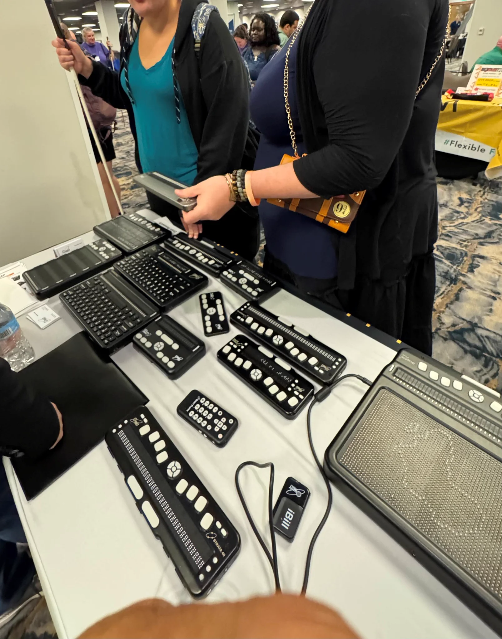 Booth visitors trying out the new Orbit Flow 40.  A number of other Orbit braille products are laid out on the table, including the Graphiti Plus, which shows a map of Africa.