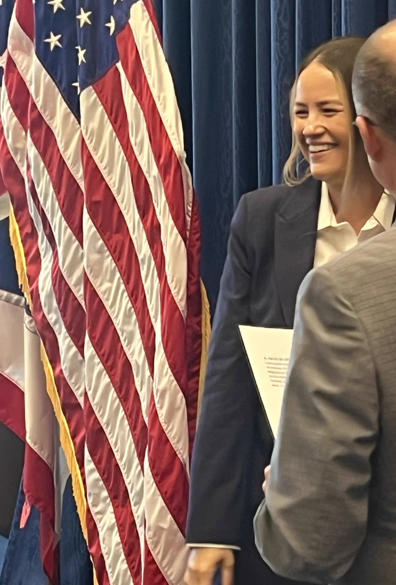 A woman is standing and smiling next a a US flag after she takes the oath of office.