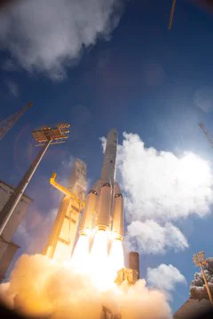 Immagine che mostra il primo lancio di Ariane 6 con booster basati sul modello P160C. Il lanciatore è staccato da terra e si alza verso un cielo azzurro con qualche nuvola bianca.