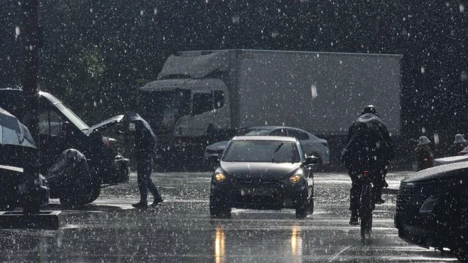 Moody urban street scene in heavy rain with cars and pedestrians.