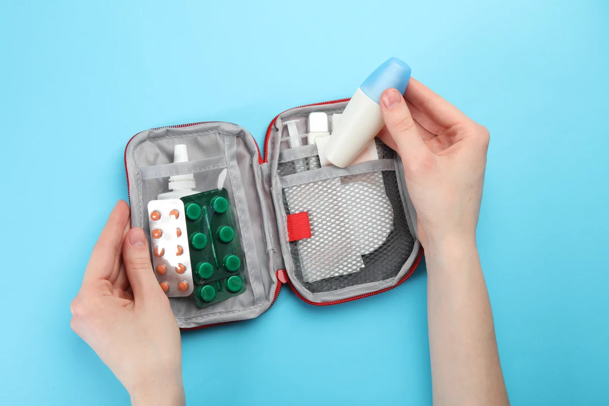 Des mains plongent dans une trousse de premiers soins ouverte pour en retirer des médicaments. 
