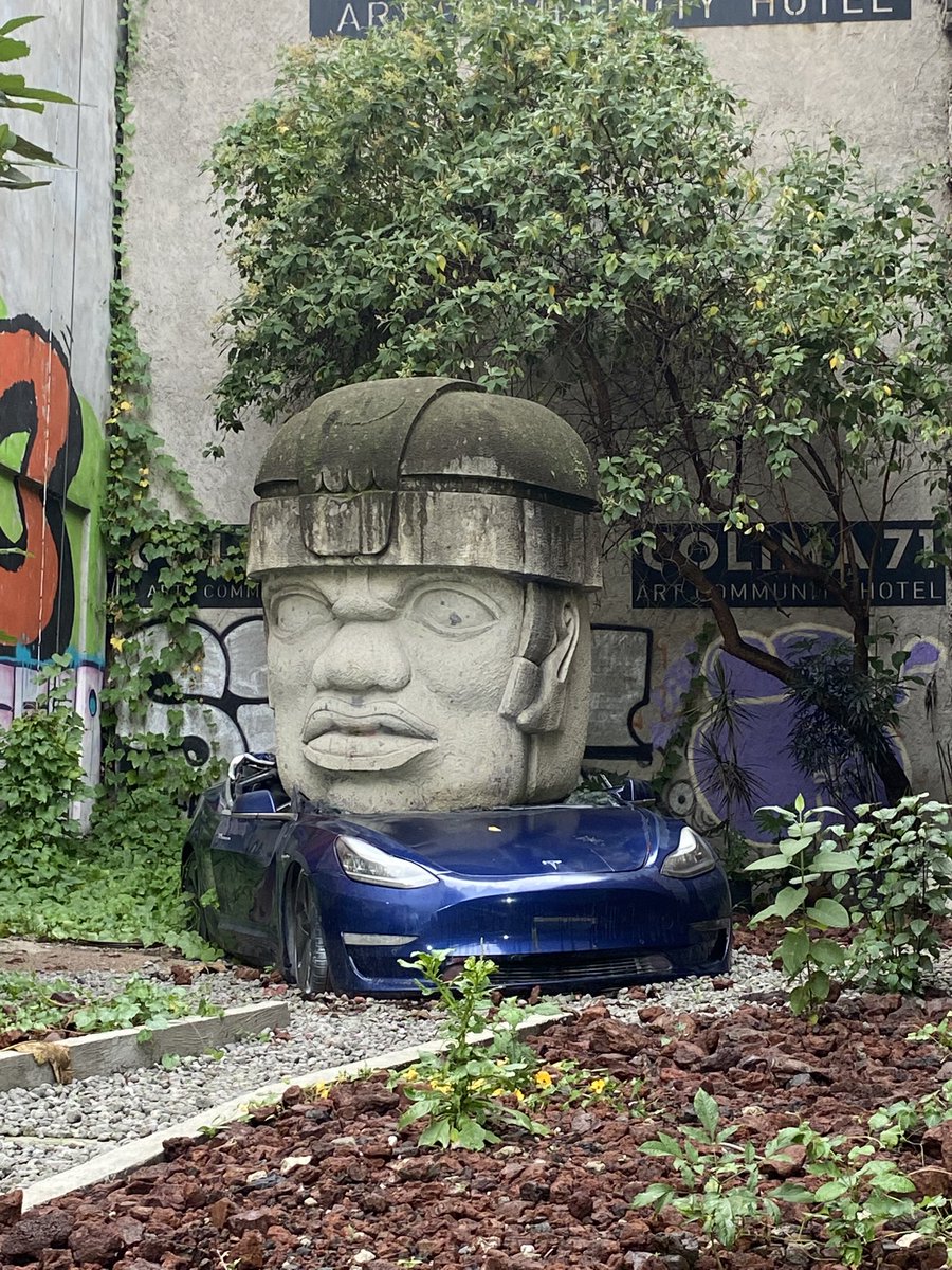 jasonachristian's tweet photo. Fascinating installation by Chavis Mármol on a random street in Mexico City. Yes, that’s a crushed Tesla beneath the head. https://t.co/LFQATcBFDh