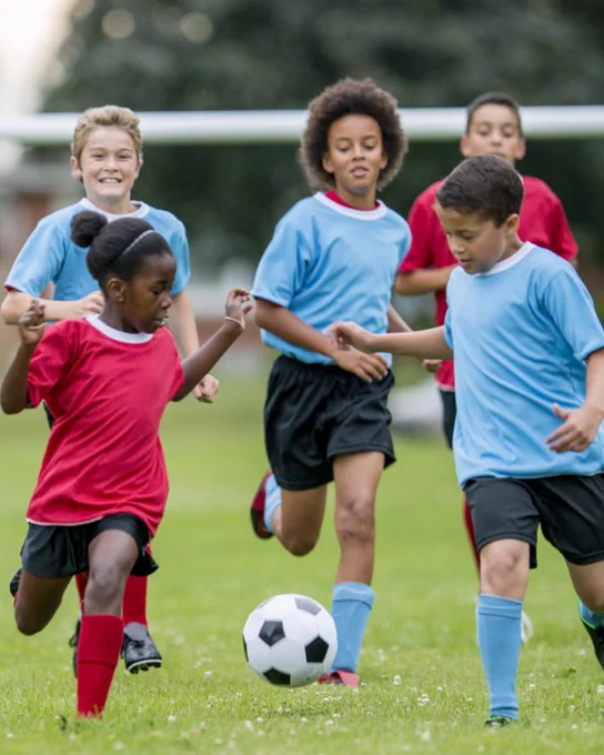 Kids in red and blue jerseys playing soccer on a green field