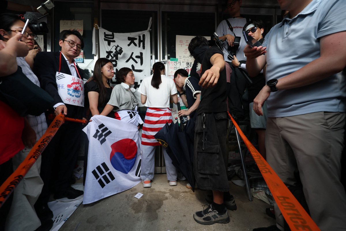 MAGAsFix's tweet photo. 🇰🇷Joan of Arc Targeted by Tyrants

South Korean police are now hunting this fearless woman in her thirties who heroically blocked an entrance for two grueling hours at the Olympic Park ballot site. She stood firm after witnessing blatant vote irregularities and denied access during the June local elections, demanding full transparency to protect every legitimate ballot. 🇺🇸Draped in the American flag, she became a symbol of defiance against fraud.

Yet authorities ignore the suspicious counting chaos and instead charge her with obstruction. This savage crackdown reveals a corrupt regime terrified of accountability, persecuting patriots while shielding the real vote manipulators. Pure authoritarian garbage that should ignite widespread fury. Stand with her before your rights vanish next.