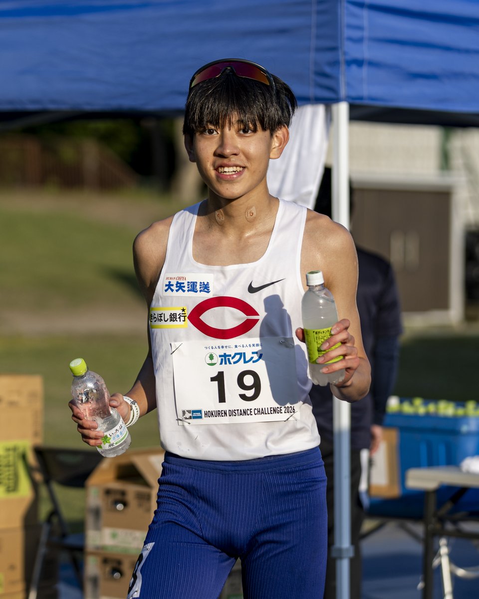 EKIDEN_News's tweet photo. 13分42秒38の台湾新。
それでも簡子傑が納得しなかった理由

ホクレン千歳5000mC組。
4着、13分42秒38。
自己ベスト、そして台湾記録更新。

それでも、中央大1年・簡子傑は納得していなかった。
こちらの姿を見つけると、
腕で大きくバツ印をつくってやってきた。
それもそうだろう。
ラスト400mまで、
終始、鼻呼吸で走っているように見えるほど余裕があった。

多くの選手たちが暑さでペースを落としていく中、
台湾南部・高雄出身の簡にとって、
北海道の夏の暑さは、高雄の春くらいに感じたのかもしれない。

「ラストのバックストレートが、思ったより伸びなかったかな？」
そう聞くと、
「前で引きすぎて、体力を使ってしまいました」
と、悔しそうに話した。

しかし、大学1年生で、シニアの選手たちを相手に、
自分でレースを動かし続けたことは大きい。
記録だけを見れば台湾新。
けれど、本人の中では、
まだまだ行けたという感覚の方が強かったのだろう。

今年の夏、簡はU20世界選手権の1500m、3000m台湾代表として、
アメリカ・ユージーンへ向かう。
さらに秋には、名古屋アジア大会1500mの台湾代表にも選出されている。
同級生たちよりも先に、世界の舞台で戦うことが決まっている。

昨年のアジア選手権でも、5000m台湾代表として走った。
台湾の中長距離界にとって、簡子傑はすでに「これからの選手」ではない。
その先に彼が見据えるのは、北京世界陸上なのだろうか。

2015年北京世界陸上で、母親が台湾代表として
マラソンを走る姿を見て、簡は陸上を始めたという。
中華圏ではよく知られた話だ。
いま、その彼が、同じ2015年北京世界陸上のマラソン日本代表として走った
藤原正和監督のもとで競技を続けている。
偶然とは思えない陸上がつないだ深い縁を感じる。

2022年12月。
台湾・高雄の陸上競技場で、簡選手のご両親と話す機会があった。

EKIDEN NEWSのトークイベントが台北と高雄であり、
台湾に滞在していたときのことだ。
その滞在中、高雄でトレーニングをしていた
デフリンピック800mの岡田海緒さんとコンタクトが取れ、練習拠点である競技場へ見学に行った。

台北も暑い。
しかし、さらに南の高雄は、無茶苦茶暑い。

そんな土地だからこそ、高雄は陸上の
短距離・中距離のナショナルクラスの選手たちの練習拠点になっているのだそうだ。
その岡田さんのトレーニンググループを指導していたのが、
中距離選手だった簡選手のお父さんだった。

「息子が仙台育英高校に留学することになりましてね」

台湾記録を次々と塗り替えている中学生がいることは、なんとなく目にしていた。
名前に「傑」という字が入っていることもあって、
大迫傑を連想し、台湾の大迫傑みたいな選手がいる、という印象もあった。

ちょうど持っていた「あまりに細かすぎる箱根駅伝」を、ご両親に差し上げた。
あまこまの表紙には、箱根駅伝に出る大学のユニフォームが並んでいる。
お父さんはその表紙を見ながら、こう聞いてきた。

「高校を卒業して陸上を続けるのだとしたら、
　大学は青山学院大がいいですかね？」

即座に答えた。

「いや、息子さんのスタイルであれば、
　中央大か東海大でしょう。」

お父さんがその言葉を覚えていたのかどうかは、わからない。
今、簡子傑が中央大のユニフォームを着て走っている。
それだけで、なんだかうれしい自分がいる。
つづきは。
13分42秒38の台湾新。
それでも簡子傑が納得しなかった理由
｜EKIDEN NEWS @EKIDEN_News https://t.co/CUJosgJCao