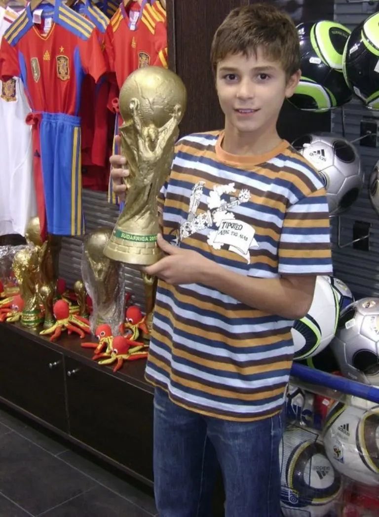 termenzo's tweet photo. Julián Álvarez de chico. Detrás, una camiseta de España y tres réplicas de Copas del Mundo. En sus manos sostiene una más. https://t.co/vnBZlN4dMq