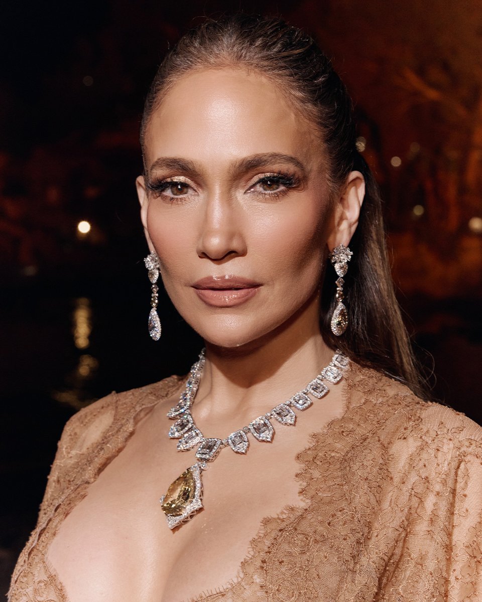 dolcegabbana's tweet photo. #JLo attended the final event of #DGAltaGioielleria, #DGAltaModa, and #DGAltaSartoria at La Plage Resort Taormina, overlooking the iconic Isola Bella, part of Parco Archeologico Naxos Taormina. She wore a look from the new #DolceGabbana Alta Moda Taormina 2026 Collection, featuring a fluid chiffon slip gown enriched with exquisitely encrusted Chantilly lace, paired with a matching chiffon robe, distinguished by voluminous sleeves intricately embellished with the same Chantilly lace. Rendered in an elegant amber nude hue. The look was completed with an exceptional Alta Gioielleria parure, featuring the Sicilian Necklace in white gold, entirely set with diamonds and centered by a 100-carat Fancy Vivid Yellow brilliant-cut diamond. Matching white gold earrings, set with colorless and brown diamonds and accented by 6-carat diamond drops, completed the ensemble. 

#DGFattoAMano