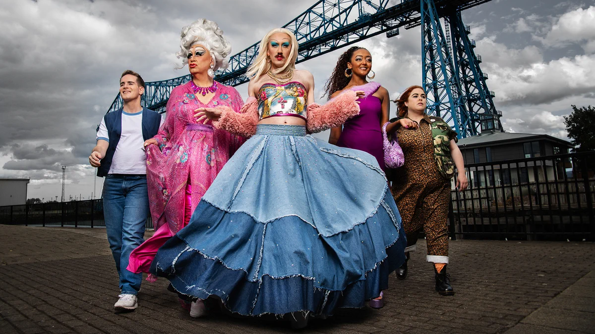 The Smoggie Queens cast lined up walking towards the camera with an industrial structure behind them