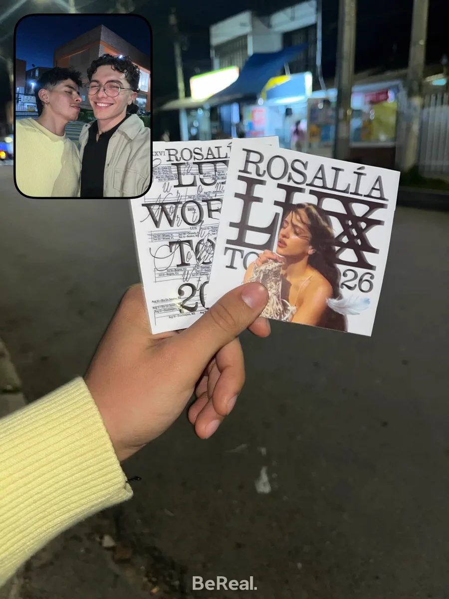 Foto BeReal. En primer plano, una mano sostiene dos boletas del tour de Rosalía 2026. En la imagen frontal se ven dos personas abrazadas y sonriendo mientras celebran que irán al concierto en Bogotá