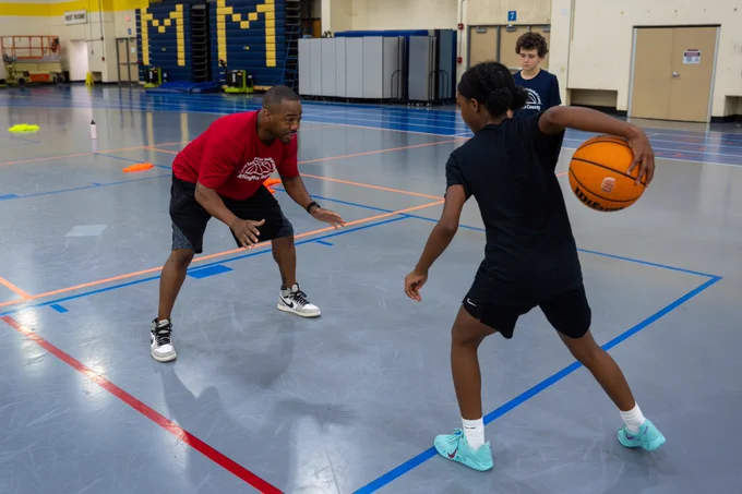 A camp counselor and a camper playing basketball one-on-one.