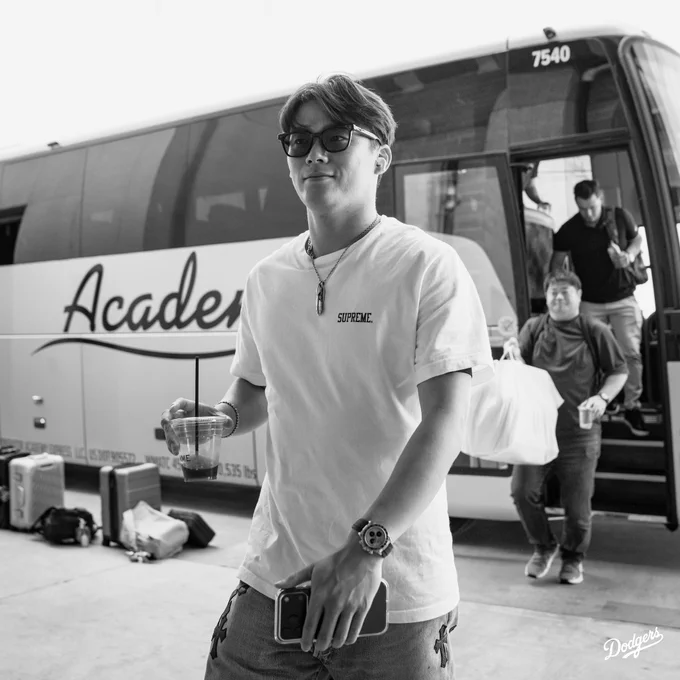 A photo of Yoshinobu Yamamoto getting off the bus and walking into the stadium while holding his coffee.