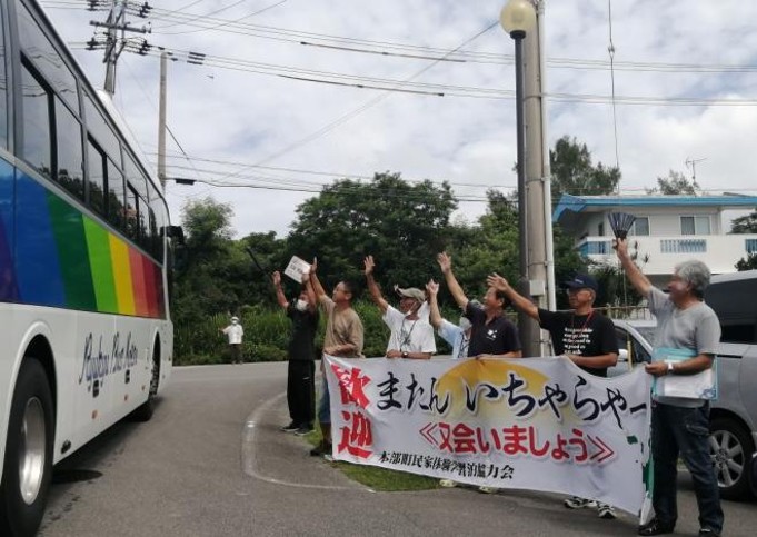 ifvoc_official's tweet photo. 【連載】「辺野古沖転覆事件」の深層（35）
「生きる力」を育てる平和学習を

沖縄の修学旅行といえば、戦跡や資料館を巡る平和学習を思い浮かべる人も多い。

しかし「教育民泊」で修学旅行生を迎えるYさん（第34回参照）は、「平和」をもっと広い視点で考えてほしいと話す。

自身は琉球政府時代やドル通貨の時代、パスポートを持っていた沖縄を経験してきた。
だからこそ、戦争だけでなく、沖縄が歩んできた歴史や文化、そして失われてきた言葉や暮らしを知ることも大切だという。

一方で、本当の平和学習とは何か。
Yさんがたどり着いた答えは、「生きる力」を育てることだった。

自分で食事を作れること。
自然の中で暮らせること。
知らない人と話し、助け合えること。
誰かと同じ時間を過ごし、人を思いやること。

教科書では学べない経験の積み重ねが、これからの社会を生き抜く力につながると考えている。

AIが進化し、社会が大きく変わる時代だからこそ、人とのつながりや生活の知恵は、ますます大切になっていく。

夕暮れ、生徒たちを乗せたバスがゆっくりと出発する。
窓を開け、「また来るね」と何度も手を振る子供たち。
Yさんも笑顔で手を振り返す。

決して楽な仕事ではない。それでも民泊を続ける。後日、Yさんのもとには、生徒たちから手紙が届く。

「民泊めちゃくちゃ緊張していたけど、時間がたつにつれて緊張がなくなって、帰るのが寂しかったです。また沖縄に来たら会いに行きます」

別の生徒はこう記していた。
「学校に行けていないことや友人関係の相談に乗ってくれてありがとうございました。Yさんの何気ない言葉で、沖縄がもっと好きになりました。これから先、心にかみしめて生きていこうと思います」

民泊で過ごした数日間は、観光では終わらない。沖縄の自然、人の温かさ、そして平和の意味を静かに噛みしめる時間となっている。

手紙を読むたび、生徒たちのはつらつとした明るい笑顔が浮かぶ。これが、Yさんの宝物だという。
（フリージャーナリスト・鴨野 守）

※写真は、民泊した生徒たちを見送る本部町民泊協会の皆さん（神奈川県立旭高校のHPより）