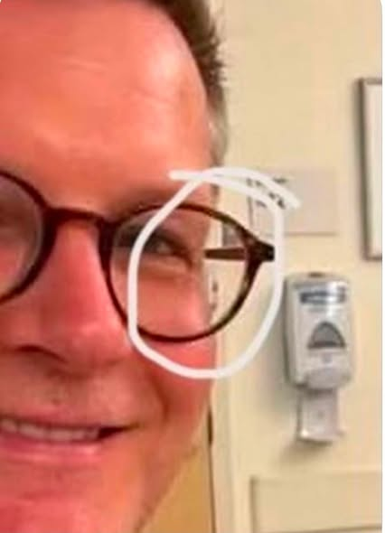 JamesTate121's tweet photo. Mitch McConnell’s team released yet another hospital photo, and apparently they forgot that some of us grew up doing the “What’s Wrong With This Picture?” puzzles in Highlights magazine.
Because I have questions. A LOT of questions.
First, why does the sign above the door appear to say Room 411 while the sign beside the exact same door says Room 412? And why are the room numbers apparently INSIDE the room?
Then there’s what appears to be a paper chart hanging from the bed. Yes, I know some hospitals still use paper for certain things, but plenty of nurses are going to look at that setup and immediately question it.  Charts aren’t beside beds anymore and haven’t been in years. If a place does use paper charts, they’re kept at the nurses station.
Now look at the IV. The bag appears full and doesn’t appear to be connected to Mitch. And what appears to be an Alaris IV pump setup looks like it has two channels but no control module—the “brain” needed to operate it.
Then I started looking around the room.
Why are there multiple hand sanitizer dispensers? Why is one positioned where it is? Why are an otoscope and ophthalmoscope mounted on the wall right beside the patient bed? Why does the angle and perspective of the bed itself look strange?
Now look at the glasses. The reflections caught my attention because what appears to be reflected in them doesn’t seem to correspond clearly with what’s around or behind the photographer. The apparent overhead lighting reflected in the glasses also doesn’t seem consistent with the way the room itself is lit.
Then there’s Mitch himself. Zoom in and parts of his face—particularly around his mouth and glasses—look strange to me. That could absolutely be compression from repeatedly uploading, downloading and screenshotting an image, but I’m looking at the entire picture, not one isolated pixel.
And after reportedly being hospitalized for weeks, he’s standing there, dressed in jeans and that familiar red checkered shirt, looking remarkably camera-ready.
Any one of these things might have a perfectly reasonable explanation. Maybe all of them do.
But when you release a photograph specifically to reassure the public that everything is fine, and I spend the next twenty minutes playing the nurse’s edition of Highlights magazine trying to figure out what the hell I’m looking at, your reassurance campaign may need a little work.
I’m not declaring the photo AI. I’m not declaring it Photoshopped. I’m pointing at the things I can see with my own two eyes and asking questions.
Because at this point, I don’t need another carefully staged photograph.
I need some answers. It's more AI slop with the same shirt on.
VIA Momma Dawn