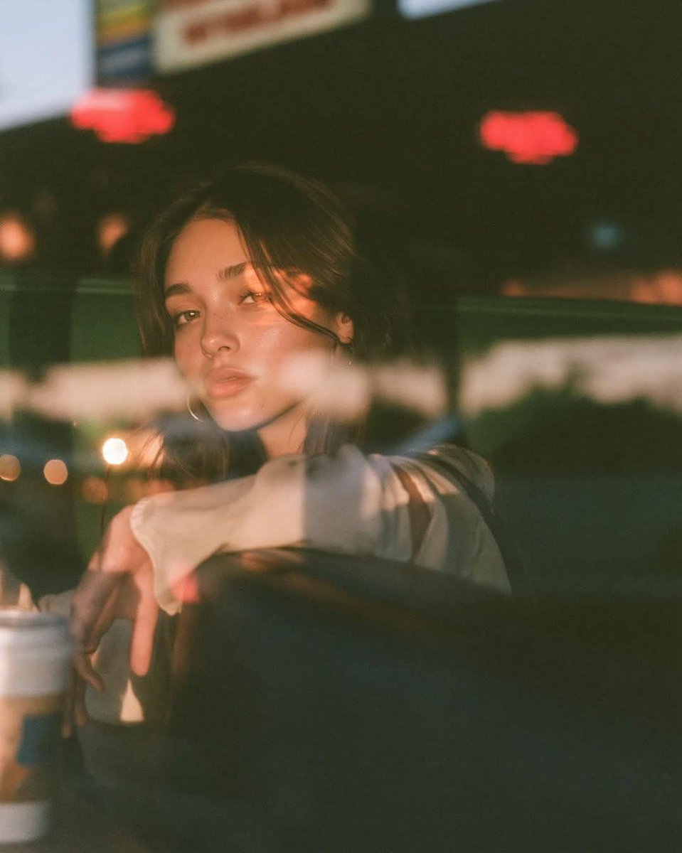 Taaruk_'s tweet photo. GPT image 2 on Chatgpt 

Prompt:
Ultra-cinematic lifestyle portrait photographed through a café window at blue hour, beautiful young woman seated alone in a cozy retro diner booth, relaxed and contemplative expression, long dark slightly messy hair framing the face, minimal natural makeup, oversized cream sweatshirt, one hand resting on the table beside a ceramic coffee cup. Shot entirely through reflective glass with layered reflections of city lights, passing cars, glowing neon signs, soft lens flares, light streaks, and subtle ghosting. Warm tungsten café lighting mixed with cool dusk ambient light creates a dreamy cinematic contrast. Rich bokeh, shallow depth of field, realistic skin texture, soft highlights on the face, moody urban atmosphere, reflections partially obscuring the subject for an editorial storytelling look. Kodak Portra 400 film aesthetic, subtle film grain, soft bloom, muted color palette, natural imperfections, Leica M11, 50mm Summilux f/1.4, photorealistic, high-end fashion editorial, intimate composition, 8K ultra-detailed, award-winning street photography, authentic candid moment.
