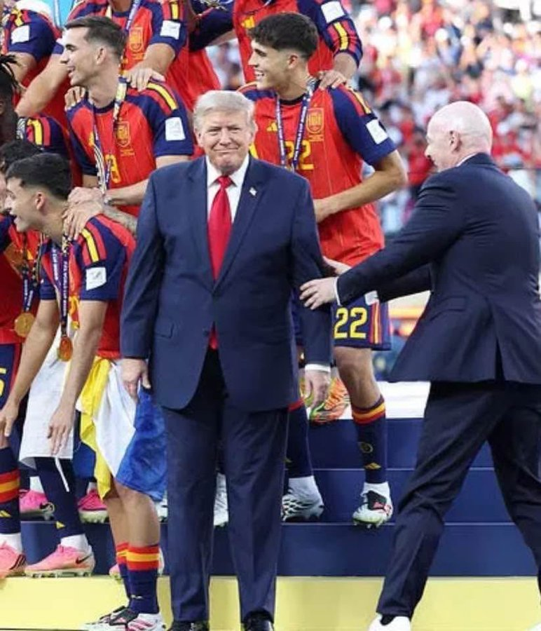 nolietees's tweet photo. According to Elon Musk's GROK 

The Spanish soccer World Cup winners did NOT ask Trump to be in the photo.

This refers to the 2026 FIFA Men's World Cup final (Spain beat Argentina).   

Trump presented the trophy as the host nation leader, but After handing the trophy to Spain’s captain Rodri, Trump LINGERED on stage and TRIED to INSERT himself into Spain’s official victory celebration photo. 

FIFA President Gianni Infantino Physically Tried to Usher him Away/Off the stage.   
(But Trump's OBESE GIRTH made the FIFA president Unable to move the large Orange Mass out of the way or risk personal physical injury)
Note: All Parenthesis commentary is NOT GROK but my own 

Back to GROK 👇

Bottom line: Trump FORCED  his way into the moment — the Spanish team did NOT invite or request him for the team photo.  

It became a widely mocked international incident.  FIFA even cropped Trump out of some official victory photos they shared afterward.“We had been told that, as a rule, Donald Trump would come to present us with the trophy and that we couldn’t lift it until he left.”

#WorldCup #Spain #ArgentinaVsEspaña  #ArgentinavsSpain #FIFA #WorldCupFinals #Trump #MAGA #patriot (🤡) #AmericaFirst #Halftime #Whitehouse #Republicans #Democrats #Independents #Soccer @POTUS @realDonaldTrump