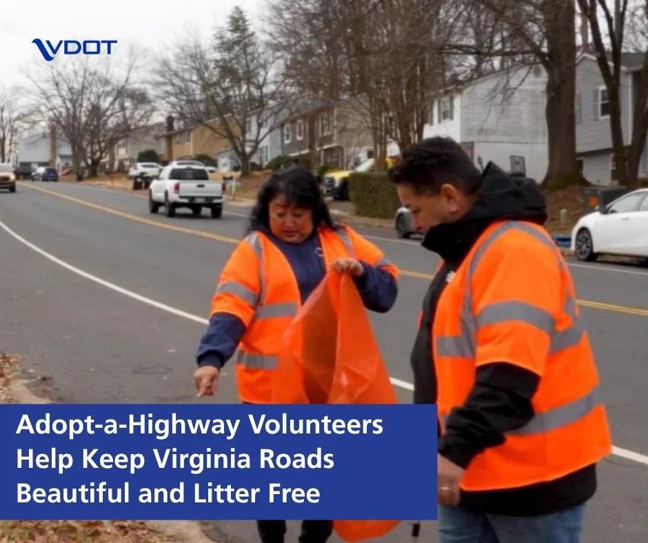 A person in an orange safety vest points to the ground on a roadside while another individual looks on. Both are holding orange bags. The scene is part of an Adopt-a-Highway initiative to keep Virginia roads clean. Houses and trees line the street in the background. The VDOT logo is present in the corner.