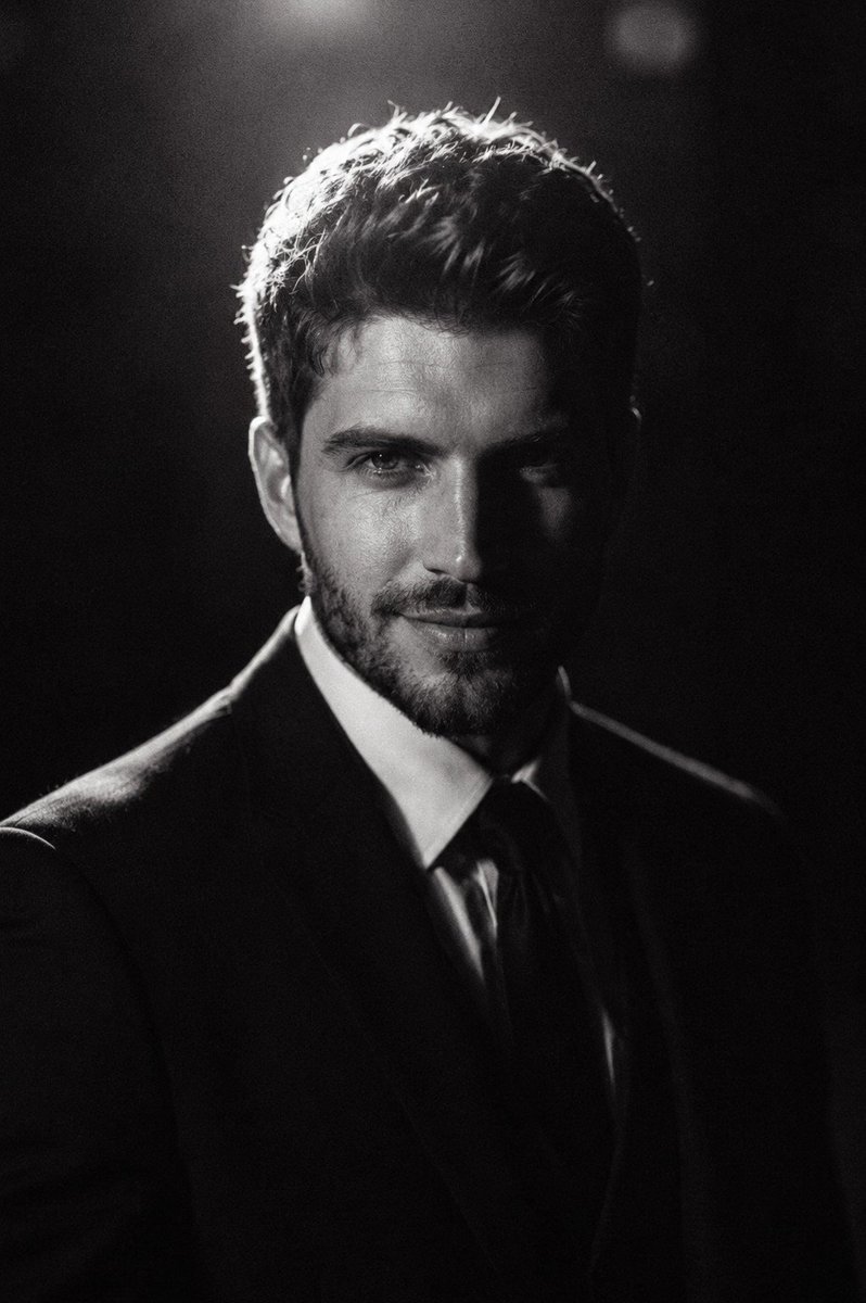 RizwanAly07's tweet photo. Gpt image 2 

Prompt ⬇️ 
Ultra-realistic cinematic black-and-white portrait of a young male in a formal black suit and tie, captured in a dark minimalist studio. Subject is slightly off-center, facing forward with a calm, serious expression and soft eye focus. Dramatic low-key lighting with a strong overhead/back light creates a glowing rim light around hair and silhouette, while the face fades into deep shadow. High contrast with smooth falloff into darkness builds a moody atmosphere. Apply heavy film grain and high ISO noise (3200-6400) for a raw analog feel. Add slight softness, subtle blur, and faint highlight bloom. Natural skin texture with visible pores. Monochrome grading with crushed blacks, soft highlights, and shallow depth of field (50mm, f/1.8).