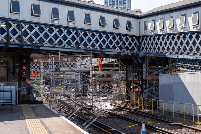 View beneath the elevated Waterloo East station walkwasy showing the structure before repainting. iT lloks old and tired, with falking paint. In the foreground you can see ailway tracks and scaffolding used for ongoing structural maintenance and refurbishment works.
