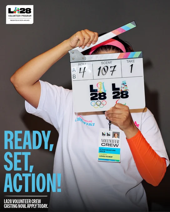 A promotional graphic for the LA28 Volunteer Crew. A volunteer holds a movie clapboard in front of their face, which features the LA28 logo. Text overlay reads "READY, SET, ACTION!" and "LA28 VOLUNTEER CREW CASTING NOW. APPLY TODAY."