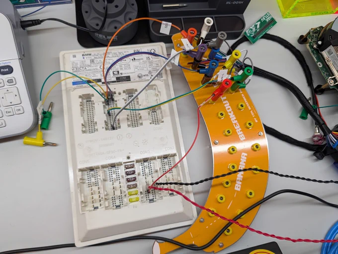 A BMW BCP ("Basic Central Platform") gateway module with a number of jumper wires connecting its various pins to a yellow banana-shaped PCB, which acts as a banana jack breakout board.