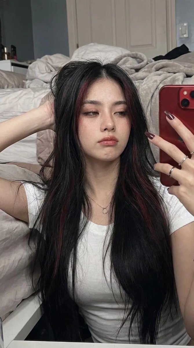 AIwithzayn's tweet photo. Chatgpt image 2 

Ultra-realistic mirror selfie portrait, vertical 9:16, captured with a high-end smartphone front camera (26mm equivalent, f/1.8, ISO 100), soft warm indoor lighting, HDR, 8K, photorealistic, ultra-detailed skin with visible pores, subtle film grain, crisp focus.
A beautiful young woman with very long, straight jet-black hair reaching below her chest, featuring subtle dark burgundy highlights on the front strands and a center part. One side is tucked behind her shoulder while the other falls naturally over the front. One hand gently brushes her hair back with slight natural motion blur, while her face remains perfectly sharp.
She has fair porcelain skin, a soft heart-shaped face, naturally full glossy lips with a soft red tint, defined arched brows with a small silver eyebrow piercing, long curled lashes, gray-green eyes, soft contour, and luminous glass-skin makeup with a subtle dewy finish.
She wears a fitted plain white stretch T-shirt, a minimalist silver circle pendant necklace, small black earrings, silver rings, and long almond-shaped dark burgundy acrylic nails. She is taking a mirror selfie with a red smartphone, wearing a relaxed, confident expression while looking slightly away from the camera.
Background: a modern bedroom with muted blue walls and a white door, softly blurred. Waist-up composition, clean aesthetic, realistic shadows, balanced exposure, premium smartphone photography, editorial quality, natural colors, identity preserved, no septum piercing, no watermark, no text.