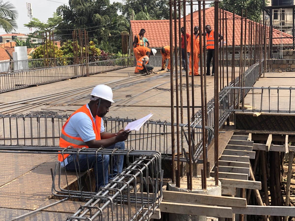 ApolloBuregyeya's tweet photo. The Engineering Behind Everyday Things.
=======
Part 16: Why Do Ground Floors Sink?
=======

A ground floor begins to sink, the tiles crack, water starts collecting in one corner, and the usual investigation committee quickly assembles. The tiler correctly blames the concrete slab, the mason blames kafeero for supplying poor quality soil backfill, Kafeero blames the plumber, and someone eventually proposes another layer of screed to raise the floor back to respectability.

That may improve the appearance temporarily, but a sinking floor is rarely suffering from a shortage of cement on top. The real problem is usually hidden underneath.

Most ground floors are built as slabs resting directly on the ground. Unlike a suspended floor, which is carried by beams, columns or walls, a ground-floor slab depends on the soil and filling material beneath it for continuous support. When that support settles, softens or is washed away, the concrete floor either follows it downwards or tries to bridge over the empty space until it cracks.

A ground floor can therefore be made from perfectly good concrete and still fail because the material beneath it was poorly prepared. A strong slab placed on weak or loose ground is rather like a good mattress placed on a collapsing bed; improving the mattress does not repair the frame underneath.

A proper ground floor normally begins by removing vegetation, roots, topsoil and other weak material. Suitable soil or crushed stone (often called fill or hardcore) is then placed and compacted before the concrete slab is cast. Each layer has a purpose, but the entire floor is only as reliable as the least disciplined layer beneath it.

One common cause of sinking is leaving topsoil or organic material beneath the building. Topsoil may appear firm during construction, but it contains roots, plant matter and other materials that decay over time. As they decompose, they lose volume and leave spaces beneath the floor.

Construction rubbish creates a similar problem. Timber pieces, empty cement bags, plastic, vegetation and loosely arranged broken blocks should not become part of the foundation simply because burying them is faster than removing them. A floor cast over a small underground landfill should not later be accused of lacking commitment.

Poorly compacted filling material is probably the most common cause. On many sites, a deep layer of soil or hardcore is dumped into the building at once, levelled and then compacted only at the surface. The top may feel firm while the material below remains loose.

Compaction equipment can only affect a limited depth effectively. It cannot transmit discipline through one metre of loose fill by telepathy. The material should be placed in manageable layers, each containing the right amount of moisture, and every layer should be compacted before the next one is added.

The type of filling material also matters. Good fill contains particles that fit together well and can be compacted into a dense, stable layer. Material containing excessive clay, large irregular pieces, rubbish or particles that crush easily may continue changing after construction.

The word hardcore is sometimes treated as though it were a professional qualification. A truck arrives carrying broken bricks, lumps of mortar, soil, timber fragments and the remains of someone’s previous construction project, and the entire mixture is promoted to “hardcore” at the site gate. Engineering requires more evidence than a confident delivery note.

Service trenches are another common source of local settlement. Pipes for water, drainage and electricity are installed below floors, after which the trenches are often filled hurriedly. If that material is not compacted carefully around and above the pipes, it settles later and creates a narrow sunken strip across the floor.

This can explain why cracks sometimes follow a straight line through several rooms. The concrete may simply be tracing the route of a poorly filled plumbing or drainage trench below it. The floor is not being artistic; it is publishing the hidden services plan.

Water can turn a small weakness into a major failure. A leaking pipe, broken drain, blocked gutter or poor ground drainage may keep the soil beneath a floor wet. Some soils become much softer when saturated, while flowing water can carry away fine particles and create empty spaces below the slab.

A leaking drain is particularly dangerous because it may remain unnoticed for years. Wastewater escapes into the ground, weakens or washes away the support, and the floor gradually sinks. By the time the tiles crack, the plumber responsible may already have changed telephone numbers and entered a different profession.

Water may also enter from outside when the surrounding ground slopes towards the building. Rainwater collects beside the walls, moves beneath the floor and changes the moisture condition of the soil. Kampala’s rain is generous, and a badly drained site can quietly redirect that generosity beneath the living room.

Clay soils create another challenge because some of them swell when wet and shrink when dry. During the rainy season, the ground may rise slightly as it absorbs water, while prolonged dry weather can cause it to shrink and lose contact with the floor. Repeated wetting and drying may therefore produce movement, cracking and uneven levels.

This movement is often more severe where moisture conditions vary across the building. Soil near a leaking pipe may remain wet while soil near an exposed external wall becomes dry. Trees can also draw large amounts of water from the ground, causing clay soils near their roots to shrink more than soil elsewhere.

Buildings constructed on sloping sites face a further risk. Part of the structure may rest on naturally firm ground while another part rests on newly placed fill. If the added fill is not properly selected and compacted, the two areas settle by different amounts.

A crack may then appear close to the line separating the cut ground from the filled ground. The building appears to occupy one plot, but the floor beneath it may be resting on two materials with very different biographies.

Heavy loads can also cause a floor to sink or crack. Domestic floors are not automatically designed to support large water tanks, heavy machinery, fully loaded storage racks or stacks of construction materials. A load that is reasonable when spread over a wide area may become damaging when concentrated through a few narrow legs or wheels.

This does not mean that every refrigerator requires a structural engineer. It means that a floor designed for ordinary household use should not later be converted into a warehouse and expected to accept the promotion without revised terms of service.

The concrete slab itself still matters. A slab that is too thin, weak, poorly reinforced or badly cured may crack more easily when support below it changes. Reinforcement can help hold cracks together and allow the slab to bridge small weak areas, but steel cannot permanently suspend an entire floor over disappearing soil unless the slab was specifically designed to do so.

Adding more reinforcement is therefore not a substitute for preparing the ground properly. Steel bars placed over loose fill may delay the visible failure, but they cannot persuade poorly compacted soil to remain where it was dumped.

The pattern of damage can help reveal what is happening. A local depression near a pipe route may indicate a leaking service or poorly filled trench, while widespread sinking may suggest generally weak or poorly compacted fill. A long crack across the floor may follow movement beneath the slab, while cracks concentrated near heavy equipment may point to overloading.

Gaps between the floor and skirting, columns or internal walls can also provide useful clues. Water collecting in areas that were previously level is another sign that the slab has moved. Cracked tiles and grout may be the first visible symptoms, but they are often only the decorative surface reporting a deeper problem.

It is also important to distinguish a sinking ground floor from settlement of the building’s foundations. Sometimes the floor moves while the walls and columns remain stable because the slab and foundations are supported separately. In such a case, gaps may form between the floor and walls without major cracking in the structure above.

If walls are also cracking, doors and windows are jamming, columns appear to have moved or the roof line is changing, the problem may extend beyond the floor. That requires a broader structural and ground investigation rather than another meeting with the tiler.

Repair should begin by finding the cause and measuring the extent of movement. Plumbing and drainage systems may need to be tested, floor levels surveyed and the material beneath the slab investigated. Breaking one tile and looking disappointed is not yet a geotechnical investigation.

Where a small void exists beneath an otherwise sound slab, specialised grouting or slab-lifting methods may sometimes restore support. These solutions only make sense after leaking water, erosion or other causes have been controlled. Filling a void while the drain continues washing away the soil simply creates a subscription service for the repair contractor.

More serious cases may require removing part or all of the slab, excavating the unsuitable material and rebuilding the floor properly. The replacement fill should be placed in controlled layers, compacted and checked before a new slab is cast. This is disruptive and expensive, which is why the few days saved during initial ground preparation often become some of the most costly days in the life of the building.

Simply adding a new screed over the sunken floor does not restore the lost support below it. It increases the weight carried by the same weak ground and may hide the problem until the new finish also cracks. The floor is raised, but the engineering argument remains exactly where it was.

Prevention begins with understanding the site. Weak soil, deep filling, former wetlands, filled pits and expansive clay require more care than firm natural ground. Where conditions are uncertain or the proposed loads are significant, proper ground investigation and engineering advice should come before excavation rather than after the tiles begin writing reports.

All vegetation and unsuitable topsoil should be removed, while service trenches must be filled and compacted carefully. Suitable fill should be placed in thin layers at the correct moisture condition, and important projects should verify the compaction rather than judging it by the sound produced when someone stamps a boot on the surface.

Drainage must keep rainwater away from the building, and pipes beneath the floor should be properly joined and tested before they disappear under concrete. The slab thickness, strength and reinforcement should then match the intended use of the space. Good construction prepares both the concrete and the ground expected to carry it.

A ground floor does not usually sink because concrete has forgotten how to be concrete. It sinks because the material beneath it was loose, unsuitable, water-damaged, overloaded or poorly prepared. The crack appears at the top, but the mistake was often buried below long before the concrete arrived.

In Part 17, we shall widen the investigation and ask: Why Do Building Foundations Settle?