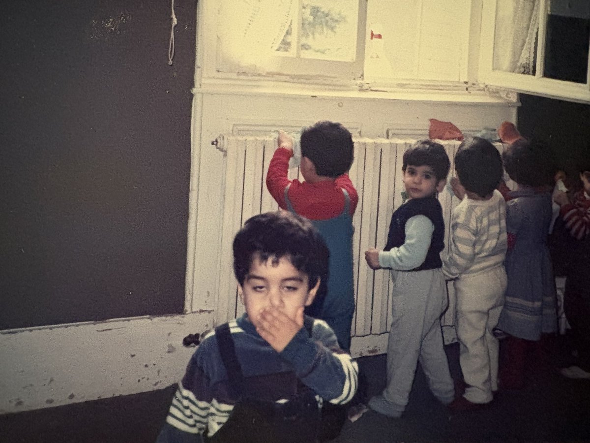 amir_yaghmai83's tweet photo. کار جمعی در سازمان مجاهدین یک ارزش محسوب می‌شد؛ تا جایی که حتی ما کودکان سه‌ـ‌چهارساله در کودکستان نیز از آن مستثنا نبودیم. تکه‌ای پارچه یا دستمالی به دستمان می‌دادند و از ما می‌خواستند شوفاژها را تمیز کنیم.

در این تصویر، من همان کودکی هستم که جلو ایستاده، پیراهن آبی به تن دارد و دستش را روی دهانش گذاشته است؛ انگار همان موقع هم از این کارهای اجباری که به کودکان تحمیل می‌شد، حالم به هم خورده بود.

این عکس حدود سال ۱۹۸۶ میلادی، در یکی از کودکستان‌های سازمان مجاهدین در پاریس گرفته شده است.