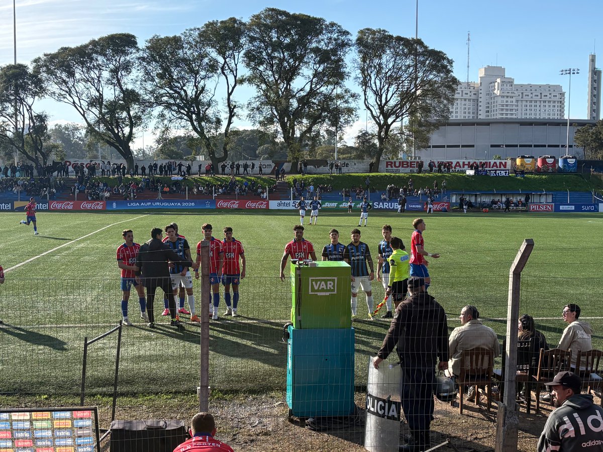 Ruxiiii4's tweet photo. Players surrounding the VAR monitor in the Uruguayan League.

Central Español vs Liverpool at Parque Palermo.

Modern technology in an old, traditional and small stadium which opened in 1937, right in the middle of a park in Montevideo.

Just a few metres from the VAR, people sit on old wooden chairs.

It all feels strangely out of place.

The football we love.