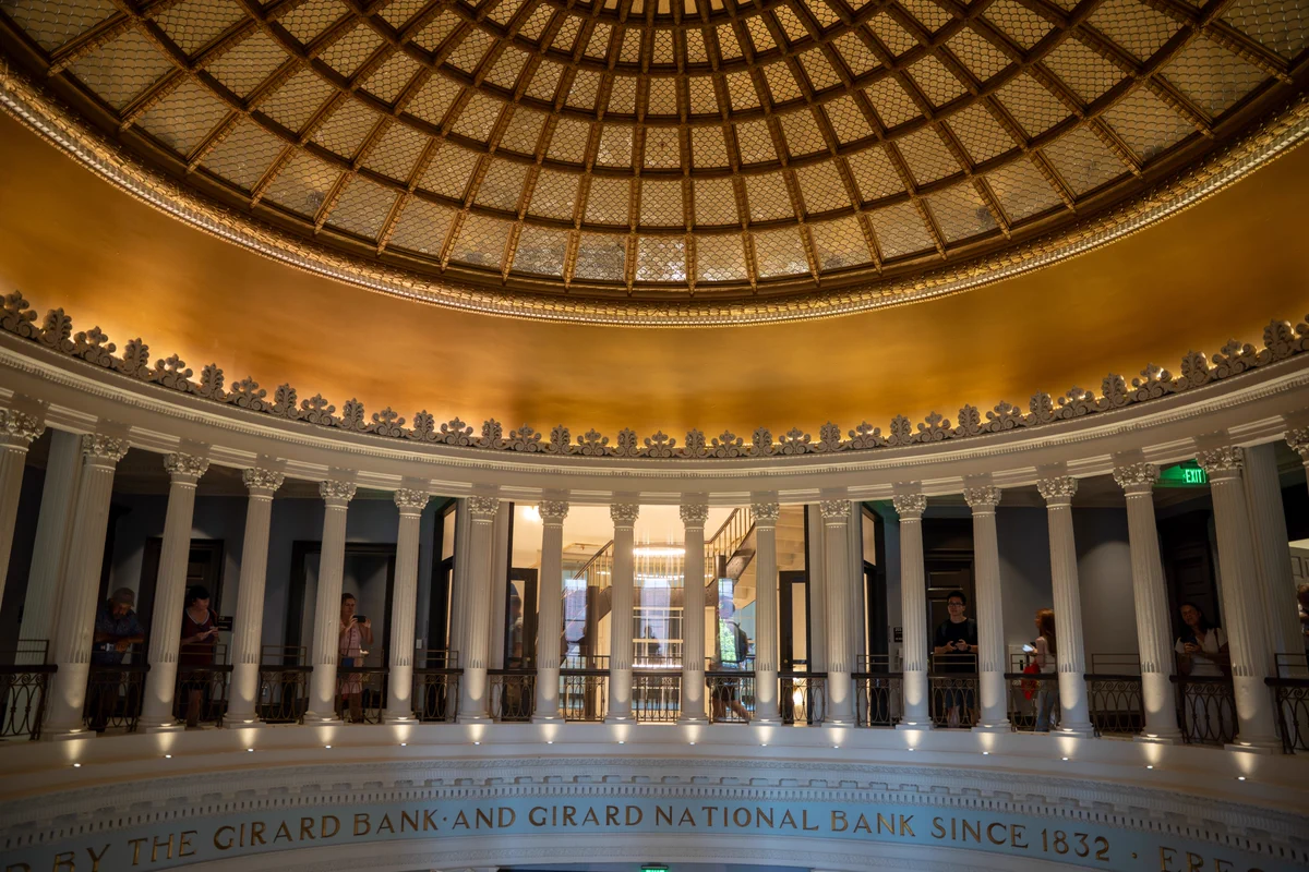 Interior view of a grand circular hall with tall columns and a patterned glass dome ceiling illuminated by warm lighting.
