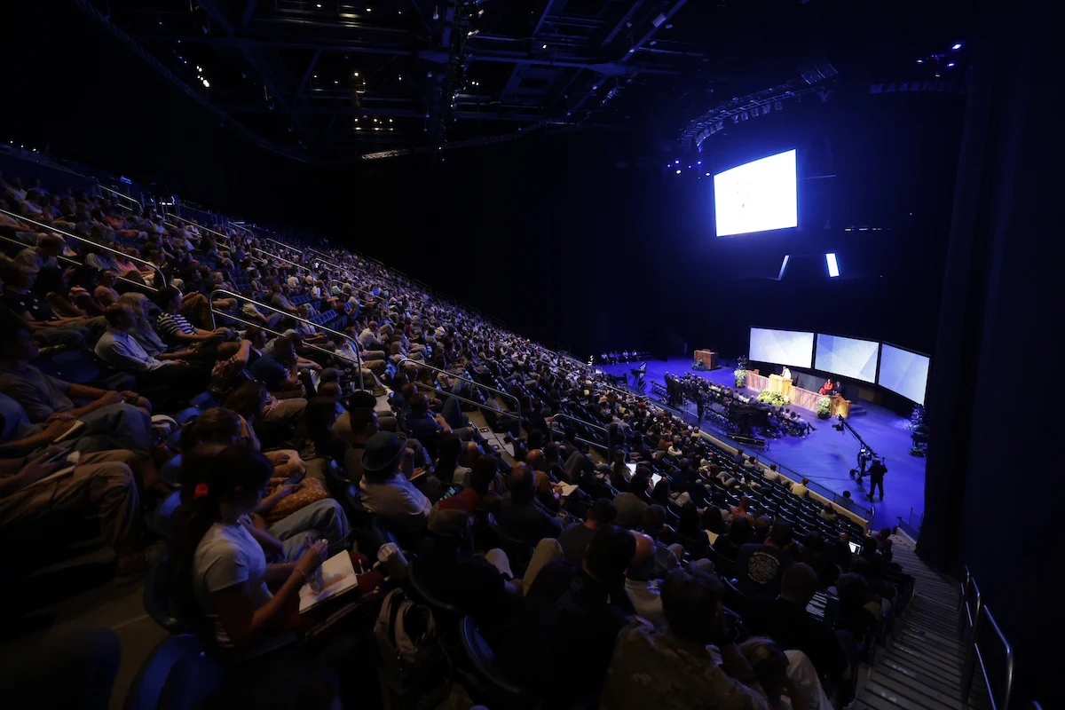 An audience in the Marriott Center is seated for BYU Devotional, August 2026
