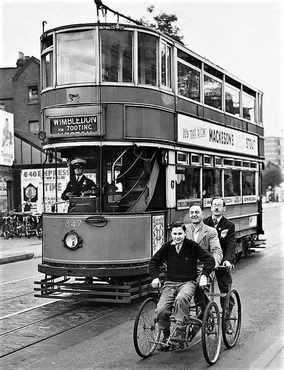 balhamnewsie's tweet photo. #ThrowbackThursday – it's #CycleToWorkDay, so what better time to share this brilliant photo of these happy travellers cycling alongside a #Tooting-bound trolleybus on #Balham High Road. Is that DuCane Court we can see in the background on the right of the photo? https://t.co/KNgCzaUyJ7