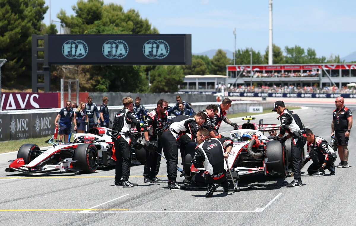 Formula 1 pit crew performing tire changes on two race cars during a sunny track session with FIA branding overhead.