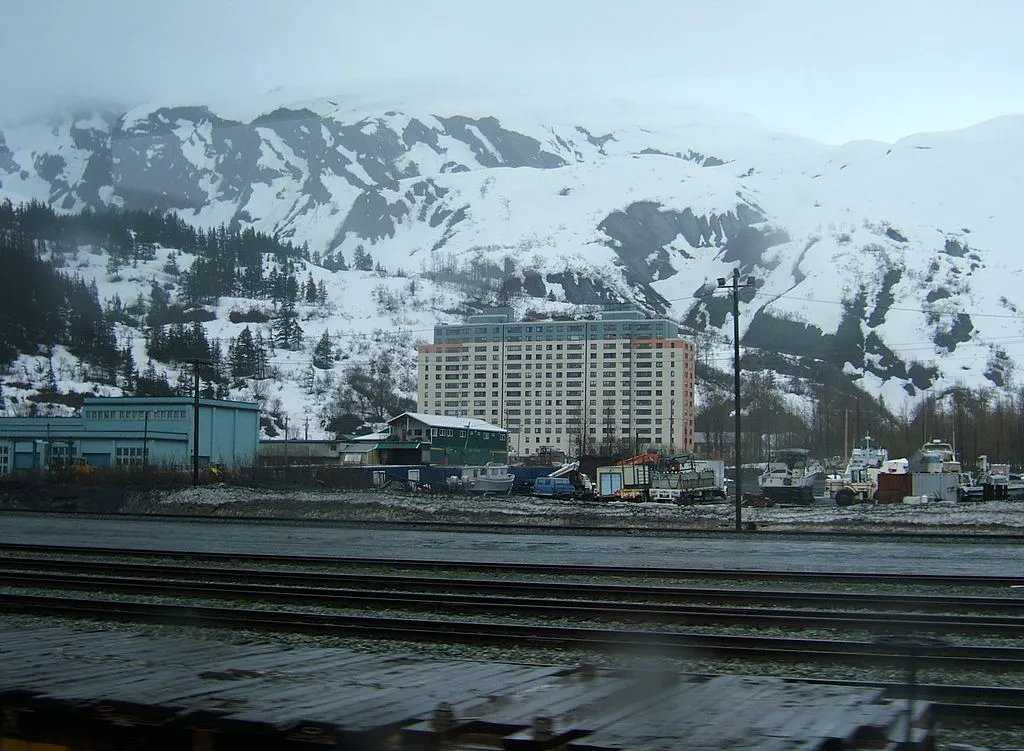 visualsofearth1's tweet photo. The Town That Lives in One Building. 🏔❄️

Deep inside a remote Alaskan fjord lies Whittier, a tiny town where most of the residents live under one roof.

The 14-story Begich Towers is home to apartments, a grocery store, post office, health clinic, church, laundromat, and the town's government offices. The local school is connected by an underground tunnel, allowing children to avoid the harsh winter weather.

Accessible through a single 2.5-mile tunnel carved through a mountain that shuts down completely at night, Whittier is one of the most unique communities in Alaska.