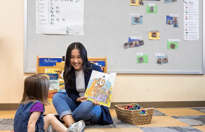 A UWM student reads a children’s book with their young child while sitting together on the classroom floor.