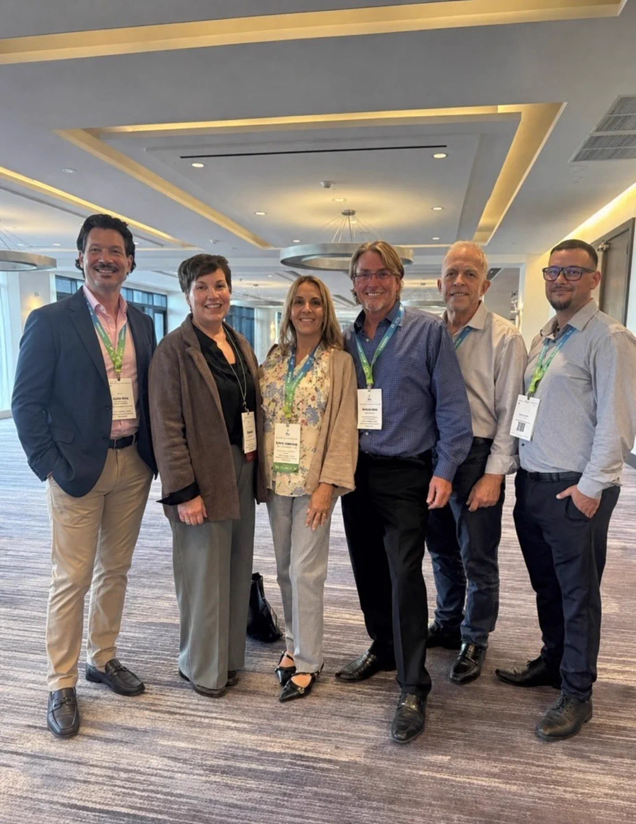 Six Care Resource professionals wearing conference badges stand together in a modern, well-lit meeting space with carpeted floors and recessed ceiling lights.