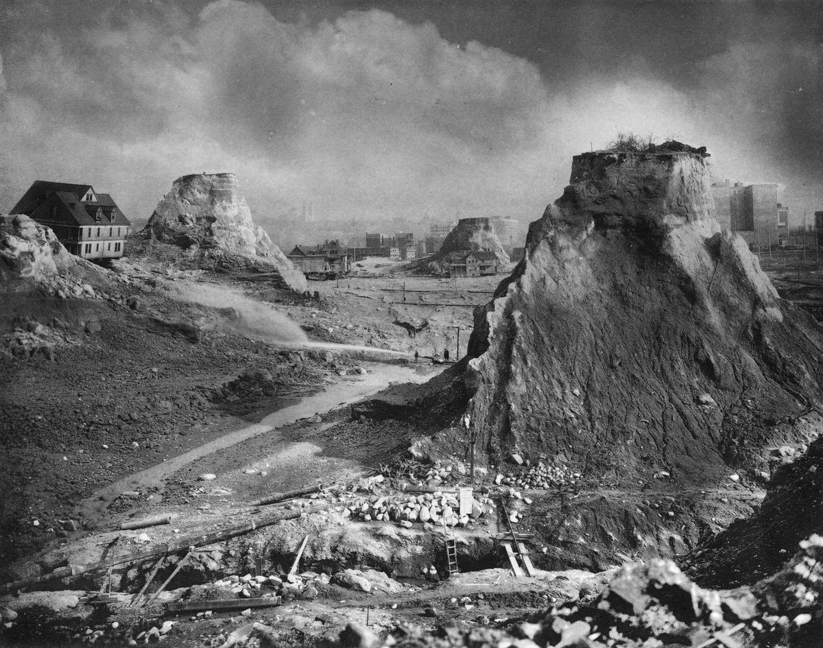 EchoesofWarYT's tweet photo. Most people have no idea that downtown Seattle used to have a hill the size of a 20 story building sitting right in the middle of it.

Denny Hill. 220 feet tall. The city looked at it and decided to just get rid of it. Not tunnel through it. Not build around it. Erase it completely.

So they pointed giant water cannons at the hill and blasted it apart with pressurized water, then washed the mud down into Puget Sound. It took them from 1897 to 1930 and they moved more than 11 million cubic yards of dirt. An entire hill, hosed into the bay.

And here is the part that sounds made up. Some homeowners refused to sell. So the engineers just carved the hill away around them. That left houses stranded on top of skinny towers of dirt, some of them a full hundred feet in the air, reachable only by a long wooden staircase. People called them spite mounds. The holdouts all caved eventually, and those last pillars got washed away too.

Now go to Chicago. In the 1850s the whole city was basically a mud pit with no drainage, so they made a decision that is hard to even picture. They raised the entire city. They put thousands of jackscrews under entire brick buildings and slowly cranked them up out of the mud, sometimes 6 feet or more. In 1860 they lifted half a city block, 320 feet of solid masonry weighing 35,000 tons, up almost 5 feet in five days, and the stores stayed open the whole time. People shopped inside while the building rose under their feet. They even jacked up a six story hotel with the guests still sleeping in it.

Boston did the opposite. The city was originally a bumpy peninsula with three big hills, which is why the main road is still called Tremont, from Trimountain. They sheared the tops off those hills, dropping the summit of Beacon Hill by around 60 feet, and used the dirt to fill in the harbor and the marshes. A huge chunk of downtown Boston is standing on ground that used to be the hills, and other parts are standing on what used to be open water.

Kansas City was so hilly and muddy they nicknamed it Gully Town, so they cut down bluffs 100 feet tall and dumped them into the ravines to flatten the place out. Los Angeles sliced whole hills out of its downtown to make room for the city core.

We walk around these cities assuming the ground was always shaped like this. It wasn't. Enormous parts of urban America were carved down, blasted apart, jacked up, and washed into the sea by men with hoses, shovels, and hand cranks, and most of it happened barely a hundred years ago.

The land you are standing on is not the land that was there.