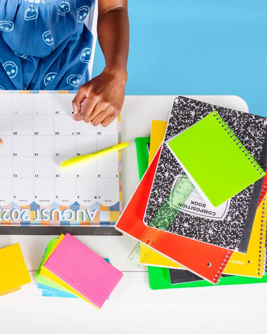 Person marking dates on an August 2023 calendar with a yellow highlighter on a white desk.