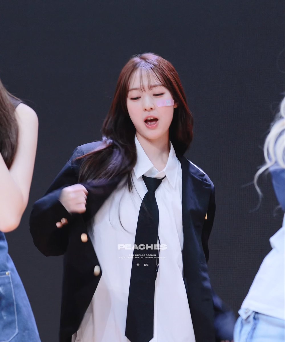 A K-pop performer with long dark hair and bangs, wearing a white shirt, black tie, and dark blazer, performing on stage; the image is watermarked 'PEACHES' with a heart and 'S6' symbol.