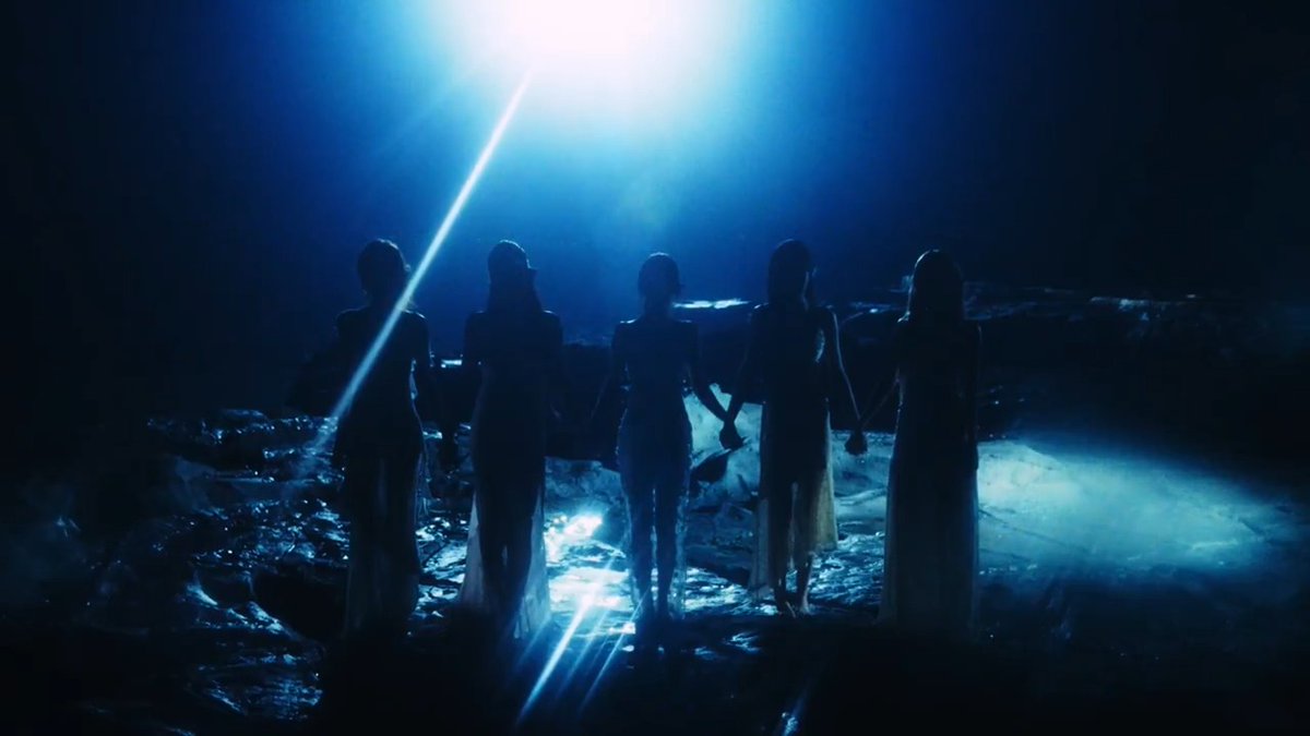 Silhouettes of five figures stand holding hands in a dark, rocky landscape illuminated by a bright blue spotlight from above.