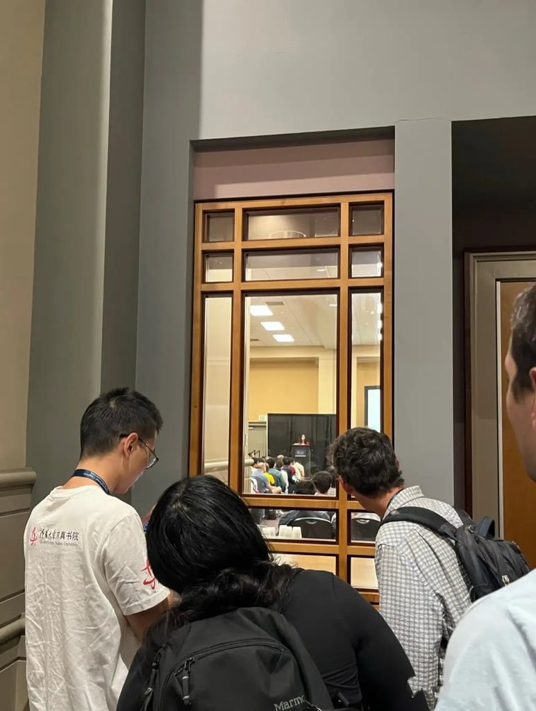xinze35794's tweet photo. 难怪王虹会特别感谢她的博士生导师拉里古斯，她在国际数学大会做报告时，拉里古斯就像在围墙边，偷看孩子在学校表演的家长一样。又得意又小心，完全不像大佬。甚至没有座位，和清华大学求真书院的代表站一起观看。

拉里古斯穿着一件随意的衬衫，背着一个破旧的包就去了，脸上挂着欣慰的笑容，就像旁观者一样，看着自己的得意门生在报告台上侃侃而谈。

王虹确实找对了土壤，不需要博士毕业后挤破头去竞争一个街道办岗位，也不需要不需要接孩子，做超纲事务，更不会被导师卡着脖子不让毕业，不通过论文。

她和导师，是互相成就，互相信任，彼此感恩的。