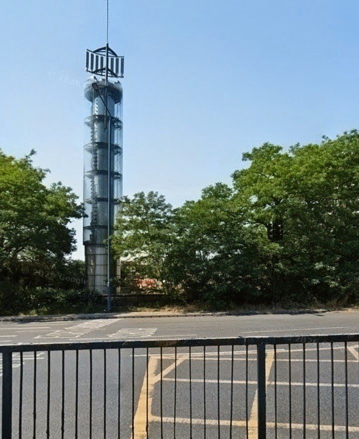 Knowledgepoint's tweet photo. The glass tube-like structure on the Holland Park Roundabout is the Thames Water Ring Main Tower, a 50-foot (15-meter) high architectural column built as a giant decorative barometer. When it was built in 1994 to mark the completion of the London Ring Main, the clear glass column was designed to display colored liquid that would rise and fall with atmospheric pressure to indicate local weather changes.  The structure is topped with communication equipment and antennae, functioning as an unorthodox mobile phone and radio mast.