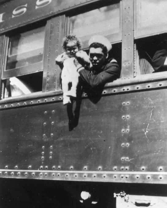 black and white photo of a sailor holding a baby out of a train window