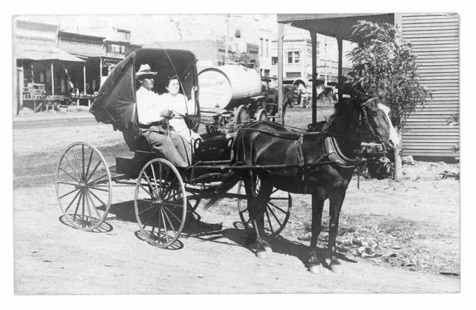 black and white photo of a man and a woman sitting in a horse drawn carriage 