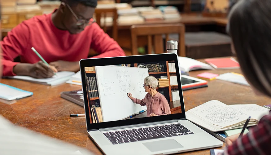 two people working at a table with a tutorial playing on a laptop screen