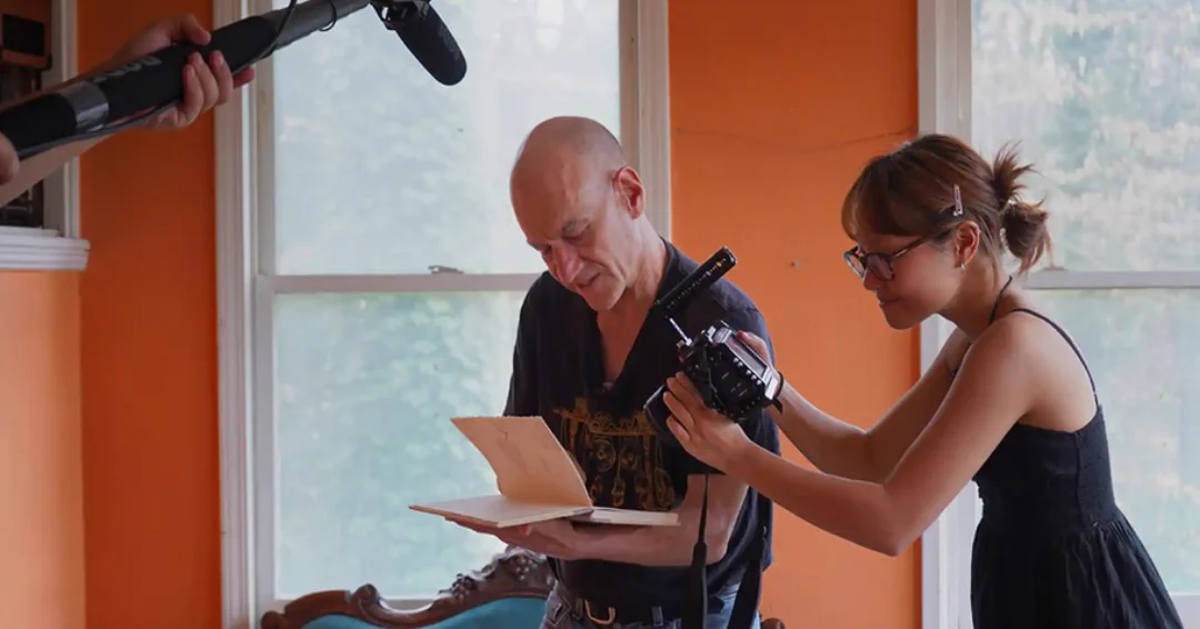 Emory alumnus Neil Fried, who founded the Railroad Earth community arts space in Emory Village, shows undergraduate Anna Zhai an old journal with a note from musician John Mayer. Zhai and three classmates are filming a documentary about Railroad Earth. 

