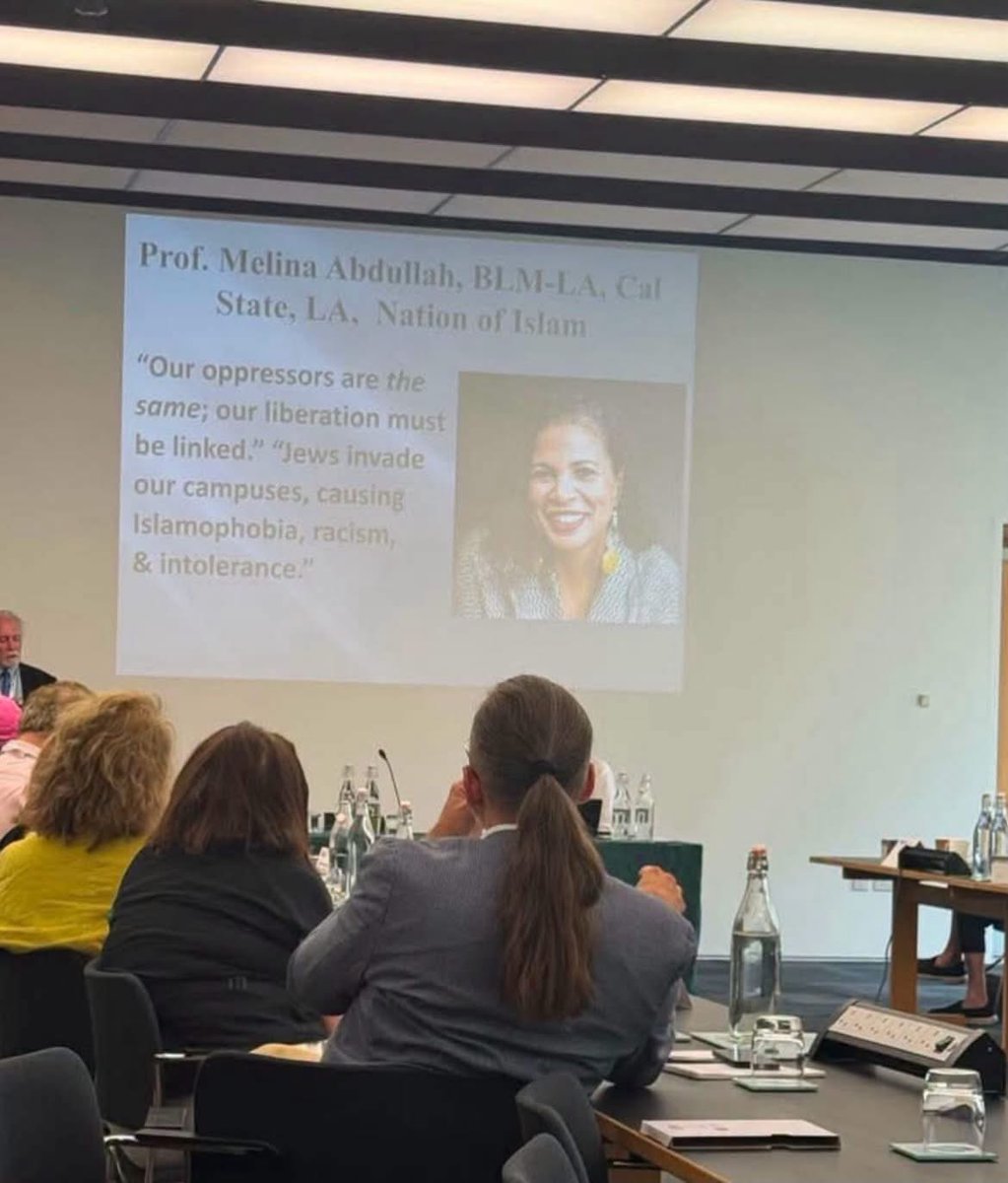 HenshiG's tweet photo. This photo is from a lecture by Professor David Patterson (University of Texas at Dallas, Holocaust scholar and ISGAP faculty) at the 2025 ISGAP-Oxford Summer Institute at St Catherine’s College, University of Oxford. 

The Institute ran late July into early August 2025. The audience is filled with scholars, educators, and researchers. Patterson was presenting the slide as a documented example of the ideology he was analyzing: the fusion of certain BLM/NOI-aligned rhetoric with classic antisemitic tropes that treat Jews as collective “oppressors” whose presence itself is framed as invasion and harm. 

Melina Abdullah is  a professor in Pan-African Studies at Cal State LA, a co-founder/leader of BLM-LA, and has longstanding public associations with the Nation of Islam. The quotes on the slide (“Our oppressors are the same; our liberation must be linked” and “Jews invade our campuses, causing Islamophobia, racism, & intolerance”) were put forward by Patterson as representative of that current.

Imagine the word “Jews” replaced by any other group.
“Blacks invade our campuses, causing…”
“Asians invade our campuses, causing…”
“Immigrants invade our campuses, causing…”
“LGBTQ people invade our campuses, causing…”
The room would empty. Careers would end. The media would burn for days. Administrators would issue statements within the hour. The moral panic would be absolute and righteous.

But when the target is Jews, the slide goes up in a professional setting, the professor keeps her post, the ideology keeps its institutional home, and too many people look away or call it “critique.”

This is not abstract. This is the language that turns Jewish students into the problem simply for existing on campus. 

It is the same poison that has made Jewish kids hide their Stars of David, take longer routes to class, and wonder whether the university that collects their tuition still believes they belong.

We have watched this logic metastasize for years. 

Intersectionality that somehow always finds the Jew as the shared oppressor. Liberation talk that excludes one people from the circle of the oppressed. “Linked struggles” that treat Jewish self-determination as the obstacle to everyone else’s freedom.

Enough.

Jewish students are not invaders. Jewish presence is not the cause of Islamophobia or racism. And a public university professor who teaches or platforms that lie — whether in a classroom, a conference, or a movement — is not engaging in scholarship. She is participating in the oldest hatred dressed up in the newest language.

We will not pretend this is complicated. We will not soft-pedal it for the sake of progressive coalitions. We will name it, document it, and refuse to let it become background noise.

The Jewish people are not going anywhere — not off campus, not out of history, and not out of the moral conversation.

Never again means never again for us, either.