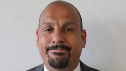 Alexandr4Denman's tweet photo. On the left a picture of Labour councillor Ricky Jones who was filmed making a slice the neck of white British so called far right people , he got a slap on the hand , of course it wasn't at all offensive to white natives because we are not allowed to be offended are we???
On the right is Reform councillor Glenn Gibbins who wrote a comical post about the pothole crisis maybe a bit dark humoured to some but a typical British humour shown and that btw was two years ago ....he's just been arrested for that ! 
TELL ME IS THAT FAIR? 
WHEN DID THIS COUNTRY GET SO WEAK THAT WORDS DESERVE PRISON 
YET A VIOLENT GESTURE DOESNT?......Thoughts?