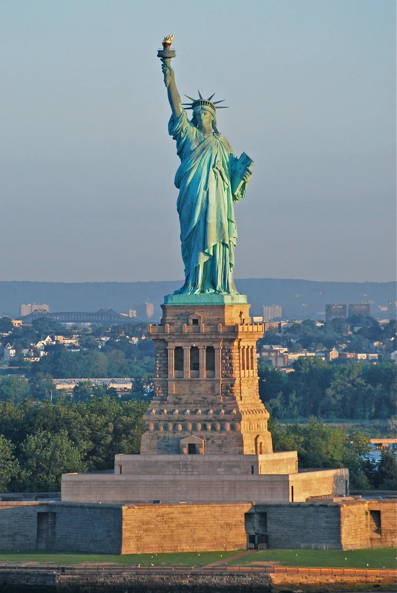 Statue of Liberty standing tall on its pedestal with a clear sky and cityscape in the background.
