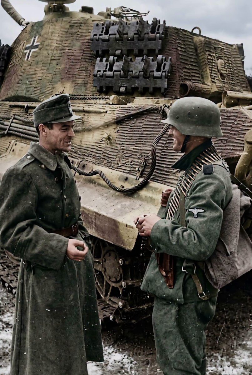 TheAxisCampaign's tweet photo. Two Wehrmacht infantry have a cigarette break next to a King Tiger tank with Zimmerit during the lull in the fighting.

The King Tiger or Königstiger is number 231 from the Schwere Panzer Abteilung 503. https://t.co/TkOBAcr8hW