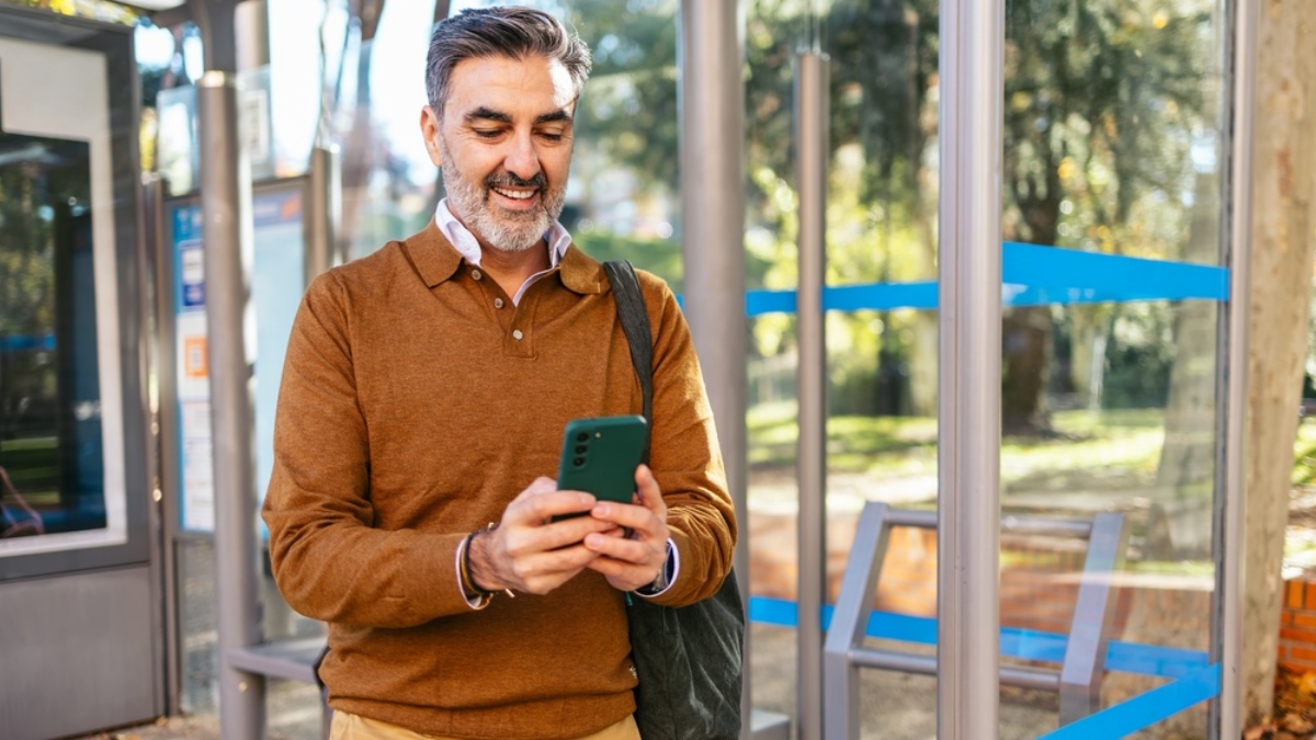 Borrower signing up for auto debit on mobile phone, tablet, or laptop while waiting at a bus stop. 
